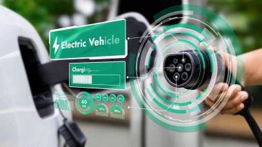 Kameranın önündeki EV şarj aletine odaklan. Bulanık arka planda akıllı batarya durum hologramını göster. Karbondioksit salınımını azaltmak için temiz enerji kullanan elektrikli araba şarjı.