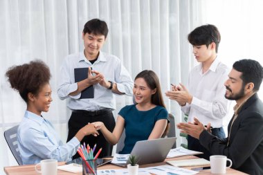 Çeşitli iş arkadaşları başarıyı şirket işyerindeki el sıkışma ve takım çalışmasıyla kutluyor. Çok kültürlü, mutlu profesyonellerden oluşan bir ekip ofiste tokalaşarak birlik oldular. Uyum