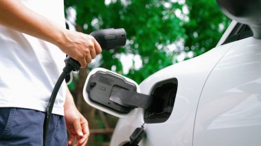 İlerici adam elektrikli aracına elektrik kablosu takıyor. Ev şarj istasyonundan EV arabası. Çevreyi korumak için temiz ve yenilenebilir enerji kullanan elektrikli bir araba. Çevre dostu otomobil.