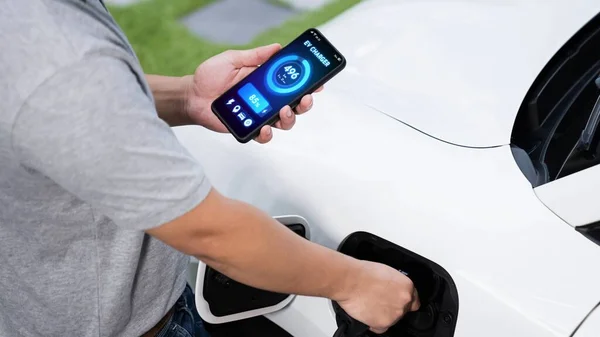 手动将电动汽车充电器插入电动汽车充电 同时检查智能手机上的电池状态显示 未来电动汽车的可持续和清洁能源 仔细阅读 — 图库照片