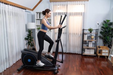 Enerjik ve güçlü atletik Asyalı kadın evde eliptik koşu makinesiyle koşuyor. Formda fiziğin takibi ve ev çalışması ve eğitimle sağlıklı yaşam tarzına bağlılık. Kuvvetli