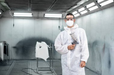 Koruyucu ekipmanlı otomotiv işçisi araba kaportasına sprey tabanca ya da oda atölyesindeki solunum boyasıyla renk boyası uyguluyor. Tamir için araba boyama servisi. Oxus.