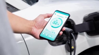 Akıllı telefon ekranı akıllı EV mobil uygulama üzerinde pil durumu EV araba garajdaki ev şarj istasyonu ile elektrik şarj ederken. Geleceğin yenilikçi EV arabası ve enerji sürdürülebilirliği. İnceleyin