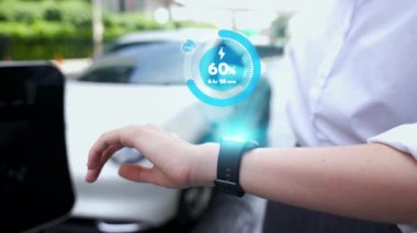 İş kadını, istasyonun otoparkından şarj olurken akıllı telefon hologramındaki EV aküsünün durumunu kontrol ediyor. EV teknolojisi adaptasyonu için temiz enerjinin gelecekteki yaşam tarzı. İnceleyin
