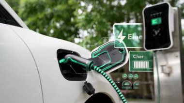 Elektrikli araba, doğal parktaki temiz enerji şarj istasyonundan gelen fütürist akıllı EV şarj cihazının dijital batarya durumu hologramıyla şarj oluyor. Gelecekçi çevre dostu EV araba. İnceleyin