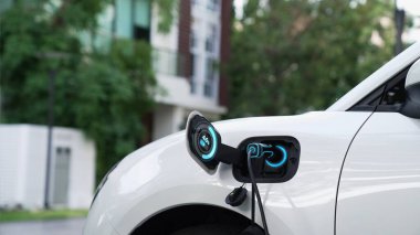Ev şarj istasyonundaki EV şarj cihazı fişe takılı ve dijital batarya durum hologramını gösteren elektrikli arabayı şarj ediyor. Akıllı ve fütüristik ev enerjisi altyapısı. İnceleyin