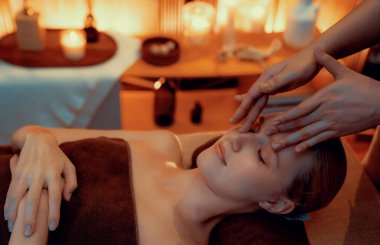 Beyaz kadın stres önleyici kafa masajı yapmaktan ve lüks otel veya otelde sıcak mum ışığında yüz güzelliği eğlencesi yapmaktan zevk alıyor. Sessiz.