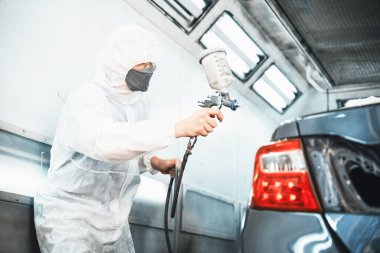 Tam korumalı ekipmanlı otomotiv işçisi sprey tabanca ya da oda atölyesindeki solunum cihazı boyasıyla araba kaportasına ustalıkla renk boyası uygular. Tamir için araba boyama servisi. Oxus.