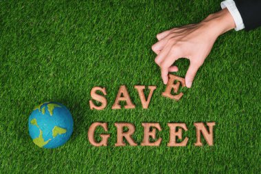 Daha yeşil ve sürdürülebilir bir gelecek için çevre korumasını desteklemek amacıyla biyofili yeşil çimen arka planı üzerine ECO ikonu tasarımı ile ekolojik farkındalık kampanyasında ahşap alfabeyi elle düzenleyin. Döngü