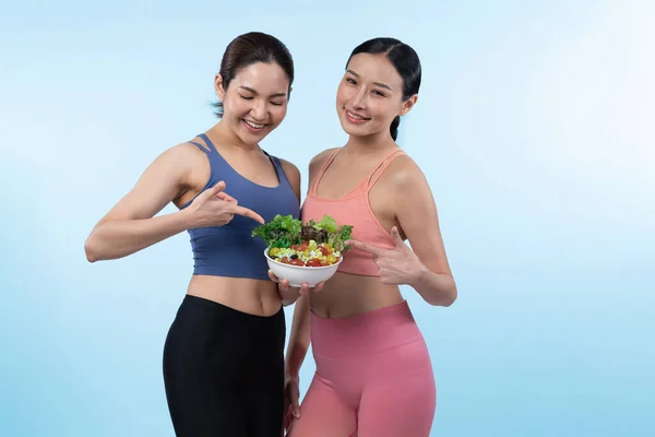 サラダボウルを保持しているスポーツウェアの2人の若いスポーティなアジアの女性は果物と野菜でいっぱいです 自然に若々しくフィットするボディライフスタイルの人々は 孤立した背景で栄養バランスをとっています ヴィゴーラス — ストック写真