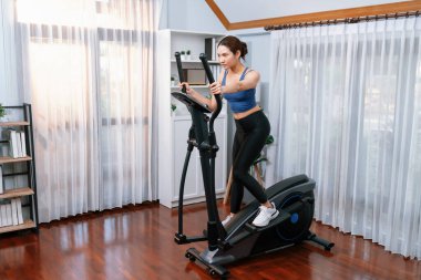 Enerjik ve güçlü atletik Asyalı kadın evde eliptik koşu makinesiyle koşuyor. Formda fiziğin takibi ve ev çalışması ve eğitimle sağlıklı yaşam tarzına bağlılık. Kuvvetli