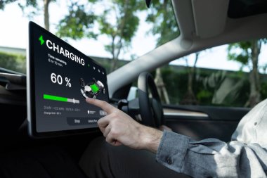 Elektrikli araba sürücüsü, arabadaki uygulama ekranında şarj durumu, menzil ve şarj limitini kontrol ediyor. Akıllı teknoloji aygıtı, EV arabasının araba aküsündeki elektrik depolama verilerini şarj ettiğini gösteriyor..