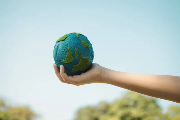Young boys hand holding planet Earth globe with sky and cloudscape background as Earth day to save this planet with ESG principle and environment friendly energy for brighter future. Gyre