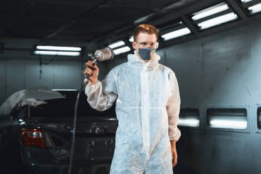 Koruyucu ekipmanlı otomotiv işçisi araba kaportasına sprey tabanca ya da oda atölyesindeki solunum boyasıyla renk boyası uyguluyor. Tamir için araba boyama servisi. Oxus.
