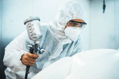 Tam korumalı ekipmanlı otomotiv işçisi sprey tabanca ya da oda atölyesindeki solunum cihazı boyasıyla araba kaportasına ustalıkla renk boyası uygular. Tamir için araba boyama servisi. Oxus.