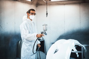 Koruyucu ekipmanlı otomotiv işçisi araba kaportasına sprey tabanca ya da oda atölyesindeki solunum boyasıyla renk boyası uyguluyor. Tamir için araba boyama servisi. Oxus.