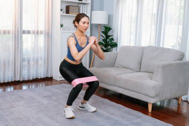 Güçlü enerjik kadın bacak kası kazanmak için direnç bandıyla evde egzersiz yapıyor. Genç atletik Asyalı kadın dayanıklılığı ve dayanıklılık antrenmanı..
