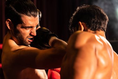 Asyalı ve Kafkasyalı Muay Thai boksörü boks maçında dirsek atağı yapıyor. Güçlü kaslı bir boksör acımasız bir dövüş hüneriyle yumruk ve dirsek yumruğa dövüşüyor. Impetus