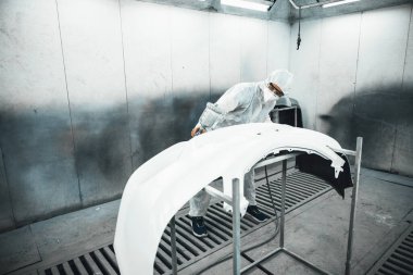 Tam korumalı ekipmanlı otomotiv işçisi sprey tabanca ya da oda atölyesindeki solunum cihazı boyasıyla araba kaportasına ustalıkla renk boyası uygular. Tamir için araba boyama servisi. Oxus.