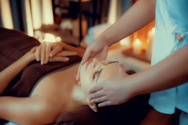 Beyaz kadın stres önleyici kafa masajı yapmaktan ve lüks otel veya otelde sıcak mum ışığında yüz güzelliği eğlencesi yapmaktan zevk alıyor. Sessiz.