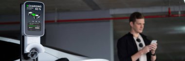 Genç adam EV elektrikli arabasıyla alışveriş merkezinin otoparkına gidiyor şehir merkezindeki şarj oluyor yeşil, temiz, yeniden şarj edilebilir elektrikli araç iç organları ile kentsel sürdürülebilirlik yaşam tarzını gösteriyor