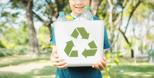 Cheerful young asian boy holding recycle symbol bin on daylight natural green park promoting waste recycle, reduce, and reuse encouragement for eco sustainable awareness for future generation. Gyre