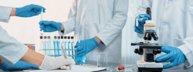 Kendini adamış bir grup bilim adamı yeni bir aşı ilacı ya da antibiyotik geliştirmek için tıbbi laboratuvarda mikroskop kullanarak kimyasal deney yapıyorlar. Biyoteknoloji laboratuvarı ve tıp araştırma konsepti. Neoterik