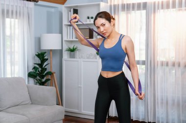 Enerjik kadın evde egzersiz yapıyor, kas kazanmak için direnç bandını esnetiyor. Genç atletik Asyalı kadın dayanıklılığı ve dayanıklılık antrenmanı ev ödevi rutin konsepti olarak..