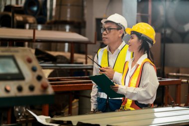 Fabrika ustabaşı ve mühendis endüstriyel çelik makinesi ve metal madde kalitesinde ürün teftişi yapıyor. Makine güvenliği ve kalite kontrollü üretim tesisi. Örnek gösteriliyor