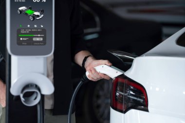 Genç adam EV elektrikli arabasıyla alışveriş merkezinin otoparkına gidiyor şehir merkezindeki şarj oluyor yeşil, temiz, yeniden şarj edilebilir elektrikli araç iç organları ile kentsel sürdürülebilirlik yaşam tarzını gösteriyor