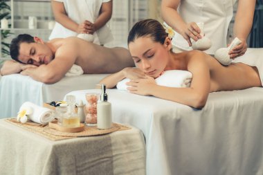 Sıcak bitkisel top spa masaj vücut tedavisi, masör nazikçe bitki torbasını çift müşteri vücuduna bastırıyor. Aromaterapi dinlenme sükuneti ve sükuneti kaplıca salonundaki atmosferi aydınlatıyor. Sessiz.