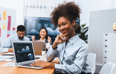 Bir grup ofis çalışanı ile birlikte arka planda ekranda gösterim paneliyle buluşan mutlu Afrikalı genç bir iş kadını portresi. Takım toplantısında kendine güveni tam bir ofis hanımı. Uyum