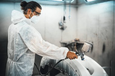 Koruyucu ekipmanlı otomotiv işçisi araba kaportasına sprey tabanca ya da oda atölyesindeki solunum boyasıyla renk boyası uyguluyor. Tamir için araba boyama servisi. Oxus.