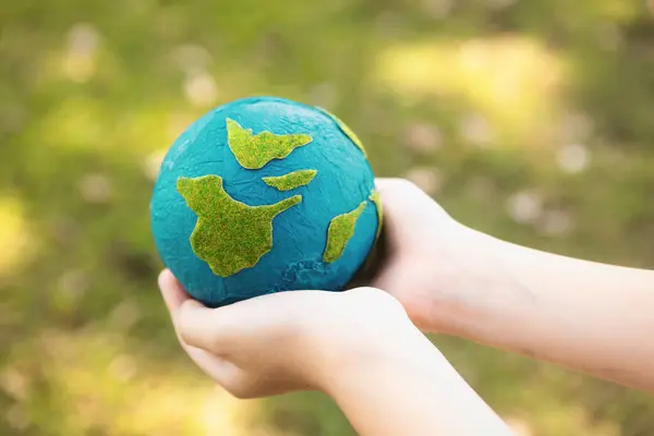 Young boys hand holding planet Earth globe at natural park background as Earth day to save this planet with ESG principle and environment friendly energy for brighter future. Gyre
