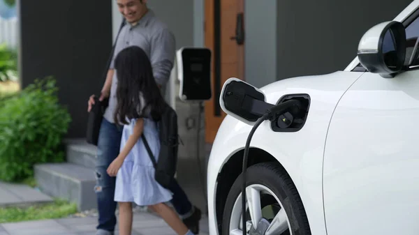 自宅で充電されている電気自動車で学校から戻ったばかりの父と娘の進歩的な概念 再生可能エネルギーによる電気自動車 — ストック写真