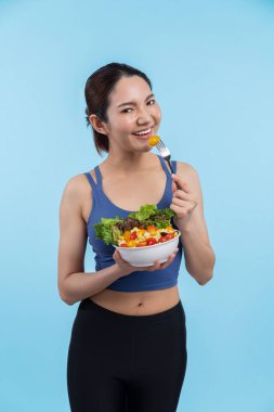 Spor giyim mağazasında elinde meyve ve sebze dolu salata kasesi tutan genç bir Asyalı kadın. Doğal gençlik ve uygun vücut yaşam tarzı izole edilmiş arka planda dengeli beslenme. Kuvvetli