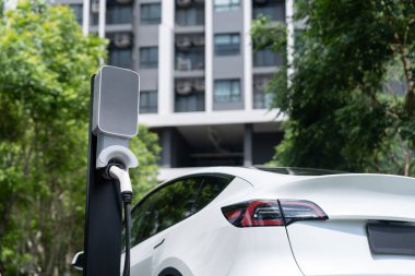 Yazın yeşil sürdürülebilir şehir bahçesinde elektrikli araba şarj oluyor. Kentsel sürdürülebilirlik yaşam tarzı yeşil temiz yeniden şarj edilebilir enerji elektrikli BEV araç iç organları