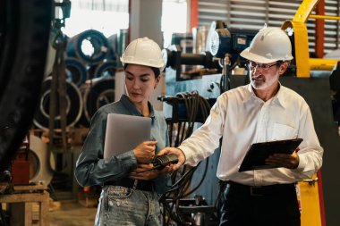 Metal imalatında makine mühendisliği denetleyicisi olarak liderlik örneğini sunan çelik endüstriyel makineyi incelemek için dizüstü bilgisayar kullanan fabrika mühendisi ve asistan..