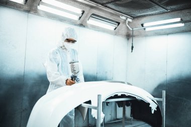 Tam korumalı ekipmanlı otomotiv işçisi sprey tabanca ya da oda atölyesindeki solunum cihazı boyasıyla araba kaportasına ustalıkla renk boyası uygular. Tamir için araba boyama servisi. Oxus.