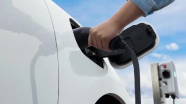 Asyalı adam şarj istasyonundan elektrikli arabaya akıllı EV şarj aleti takıyor. EV araba konseptiyle sürdürülebilir ve temiz ulaşım teknolojisi için gelecekteki alternatif enerji kullanımı. İnceleyin