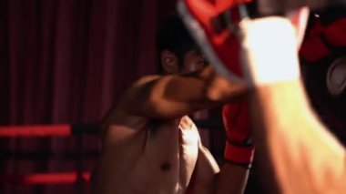 Asyalı ve Kafkasyalı Muay Thai boksörü boks antrenmanında boks antrenmanında boks antrenörüne yumruk atma, Muay Thai boks tekniği ve becerilerini sergileme. Impetus