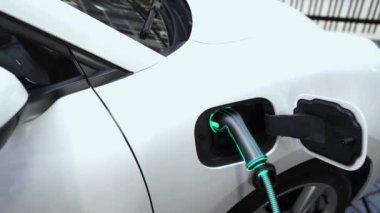 Akıllı telefon akü durumu arayüzünü elinde tutan iş kadını akıllı EV mobil uygulama ile otomobil parkındaki şarj istasyonundan elektrik şarj eden çevre dostu EV araba. İnceleyin