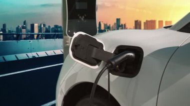 Elektrikli araç, EV araba şehir merkezindeki şarj istasyonunda şarj oluyor. Etrafı yüksek gökdelenlerle çevrili. Çevre dostu yenilikçi temiz enerji kavramı.