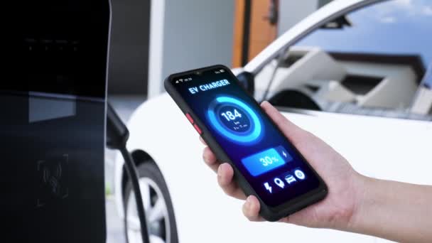 スマートフォンはスマートEvモバイルアプリケーションのバッテリーステータスを表示し Ev車はガレージ内の家庭用充電ステーションで電気を充電します 将来の革新的なEv車とエネルギー持続可能性 Peruse — ストック動画