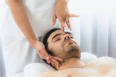 Beyaz adam stres önleyici kafa masajından ve lüks bir tatil beldesi veya otel spa salonundaki modern ışık ortamında yüz güzelliği eğlencelerini şımartmaktan hoşlanıyor. Sessiz.