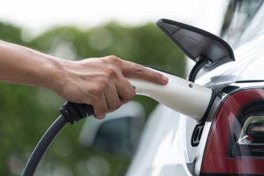 Yakından el yerleştirme ve şarj etmek için EV şarj cihazı şarj istasyonundan şarj ediliyor. Alternatif enerji, gelecekteki sürdürülebilirlik için çevre dostu taşımacılığında kullanılıyor. Eşzamanlama