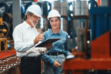 Metal imalatında makine mühendisliği denetleyicisi olarak liderlik örneğini sunan çelik endüstriyel makineyi incelemek için dizüstü bilgisayar kullanan fabrika mühendisi ve asistan..