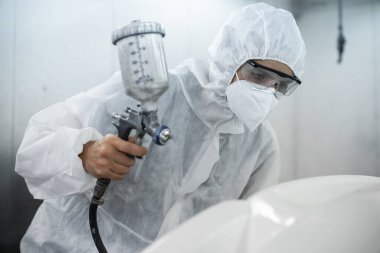 Tam korumalı ekipmanlı otomotiv işçisi sprey tabanca ya da oda atölyesindeki solunum cihazı boyasıyla araba kaportasına ustalıkla renk boyası uygular. Tamir için araba boyama servisi. Oxus.