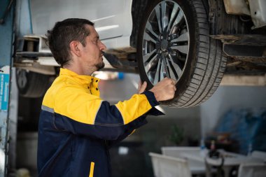 Araba kaldırma istasyonunun altında çok çalışan bir tamirci araba tekerleğini değiştiriyor. Otomotiv işçisi lastik lastiği değiştiriyor. Profesyonel araba bakımı ve bakımı konseptinde. Oxus.