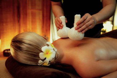 Sıcak bitkisel top spa masaj vücut tedavisi, masör kadın vücuduna nazikçe şifalı bitki torbası bastırıyor. Aromaterapi tesisinin sakinliği ve dinginliği kaplıca salonundaki mumların sıcacık ışığında. Sessiz.